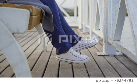 The legs of a woman sitting on a park bench in white sneakers The legs of a woman sitting on a park bench in white sneakers 79244793