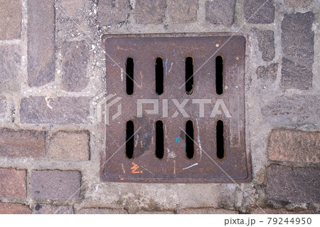 Drain hatch in the form of a grate on the road laid out with tiles. Drain hatch in the form of a grate on the road laid out with tiles. 79244950