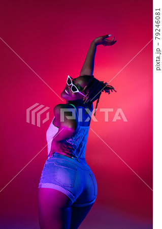 Young pretty African girl in sunglasses dancing on heels isolated on gradient studio background in neon light. 79246081