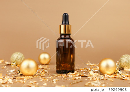 Dropping essential oil in glass bottle, Christmas balls and pieces of gold paper firecracker on golden background, new Year party. Serum with hyaluronic acid in brown glass bottle. Mockup, front view. Dropping essential oil in glass bottle, Christmas balls and pieces of gold paper firecracker on golden background, new Year party. Serum with hyaluronic acid in brown glass bottle. Mockup, front view. 79249908