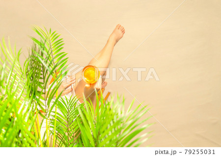Alone woman sitting under palm tree branches with glass of water with piece orange. Female relaxation on the sand of the beach at summer vacation. Top view 79255031