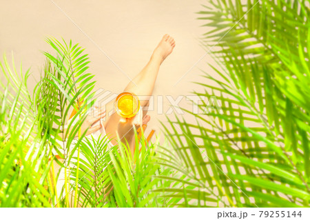 Alone woman sitting under palm tree branches with glass of water with piece orange. Female relaxation on the sand of the beach at summer vacation. Top view Alone woman sitting under palm tree branches with glass of water with piece orange. Female relaxation on the sand of the beach at summer vacation. Top view 79255144