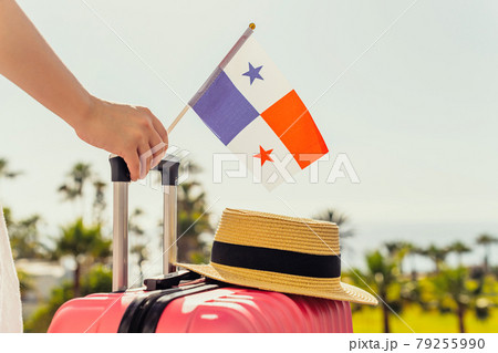 Woman with pink suitcase, hat and Panama flag standing on passengers ladder and getting out of airplane opposite sea coastline with palm trees. 79255990