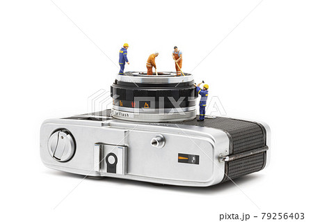 Miniature people cleaning old camera lenses on white background. 79256403