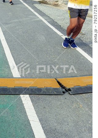 Black and yellow heavy plastic covers for people and vehicle to cross over cables laid on road. Pavement pads to protect electrical wiring on sidewalk in public park. Channel for laying the wires. 79257256
