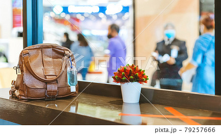 Mini portable alcohol gel bottle to kill Corona Virus(Covid-19) hang on a brown leather shoulder bag on counter in coffee shop.New normal lifestyle. Health care concept. Selective focus on alcohol gel 79257666