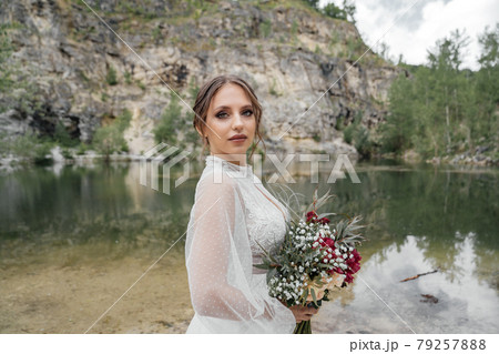 close up. The bride in a white dress with a red bouquet on the bank of a river . close up. The bride in a white dress with a red bouquet on the bank of a river . 79257888