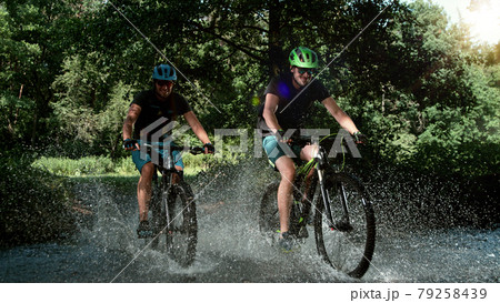 Mountain bikers speeding through forest stream. 79258439