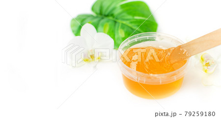 Sugar paste or wax honey in a transparent jar and white orchid on a white background. Sugaring. Depilation and beauty concept. Waxing. 79259180