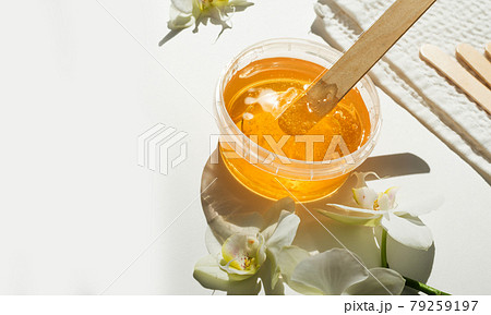Sugar paste or wax honey in a transparent jar and white orchid on a white background. Sugaring. Depilation and beauty concept. Waxing. 79259197