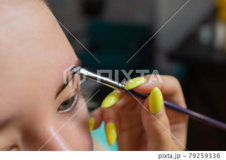 Beautician making depilation with wax strip young woman's eyebrows in spa center. Attractive woman getting facial care at beauty salon. 79259336