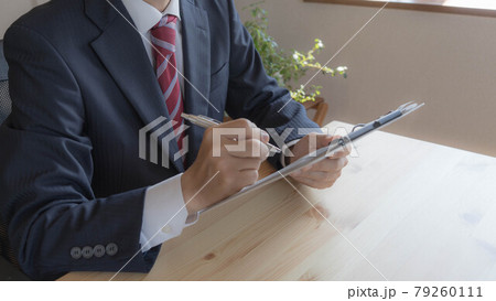 クリップボード上の書類に書き込む男性。 79260111