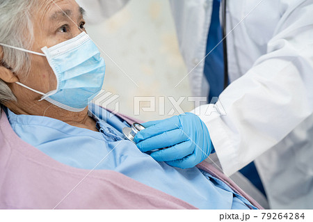 Doctor using stethoscope to checking Asian senior or elderly old lady woman patient wearing a face mask in hospital for protect infection Covid-19 Coronavirus. 79264284