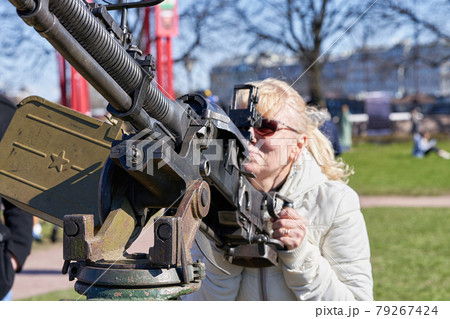 blonde woman in dark glasses shoots an anti-aircraft machine gun aiming upwards 79267424
