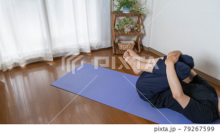部屋でヨガをする男性。胎児のポーズ(ピンダーサナ)。下半身・大殿筋のストレッチ。 79267599