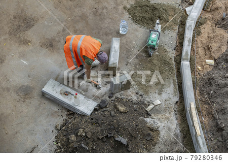 Man in orange vest while installing street curbstone Man in orange vest while installing street curbstone 79280346