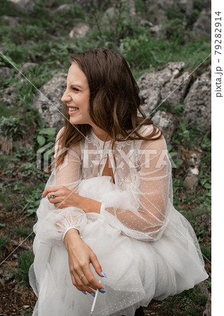 A cheerful young woman with a cigarette laughs and smokes in the woods.  79282914