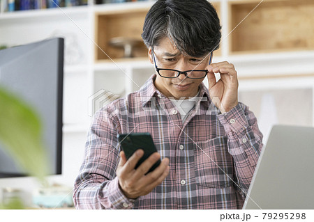 老眼鏡をずらしてスマホの画面を見る50代の男性 79295298