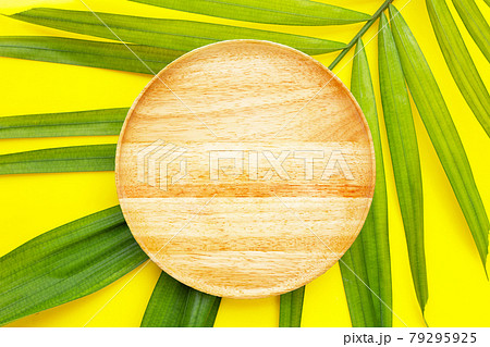 Empty wooden plate on tropical palm leaves on yellow background. 79295925