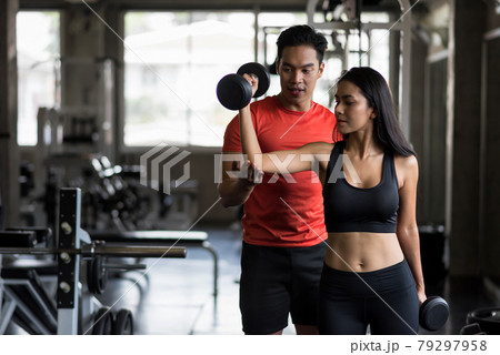 trainer set biceps dumbbell position to girl in gym 79297958