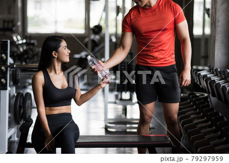 man give water to young fit woman in gym 79297959
