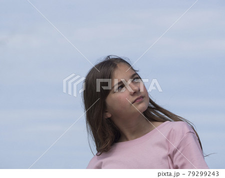 A beautiful, thoughtful girl looks up into the distance. Soft blue sky in the background A beautiful, thoughtful girl looks up into the distance. Soft blue sky in the background 79299243