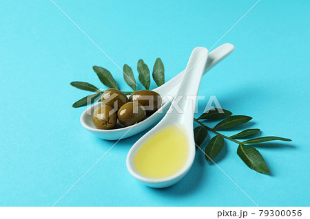 Spoons with olives and oil, and twigs on blue background Spoons with olives and oil, and twigs on blue background 79300056