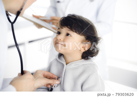 Woman-doctor examining a child patient by stethoscope. Cute arab toddler at physician appointment. Medicine concept 79303620