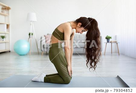 Side view of young fit Indian lady doing backbend, performing exercises for her spine health at home, full length 79304852