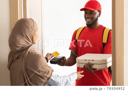 Smiling deliveryman holding POS machine, woman paying with card 79304952