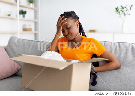 Disappointed black woman unboxing her delivery, looking inside wrong box, touching her forehead in frustration 79305145