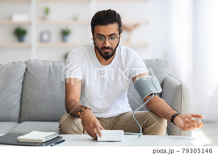 Young Man Sitting On Sofa Checking Blood Pressure At Home 79305146