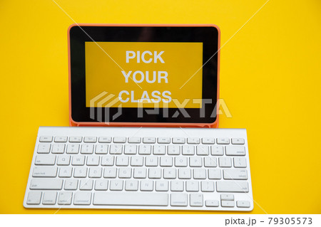 PICK YOUR CLASS text on digital tablet screen with wireless keyboard isolated on yellow background	 79305573