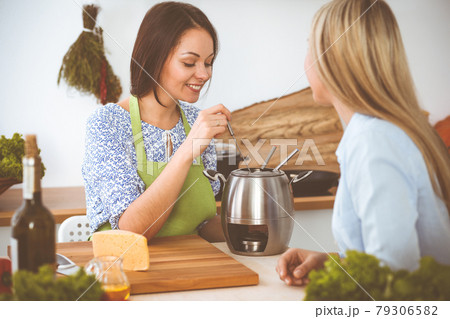 Two women friends taste new recipes for delicious fondue while sitting at the kitchen table. Healthy meal cooking concept 79306582