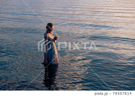 teen girl in a dress by the sea enters the water 79307614