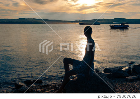 teen girl sitting on the banks of the river, looking at the ships 79307626