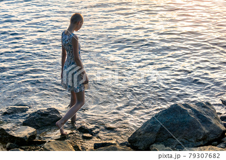 teen girl in a dress by the sea enters the water 79307682