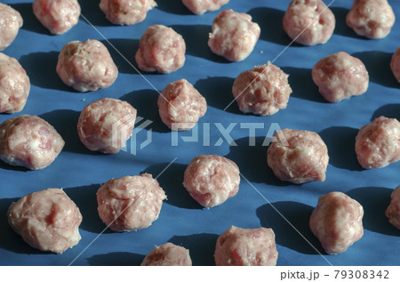Raw shaped meatballs in sunbeams on blue. 79308342