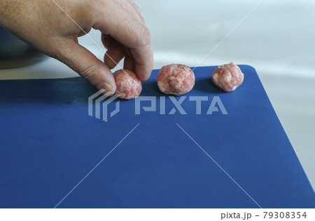 Male hand puts meatballs on a blue surface. 79308354