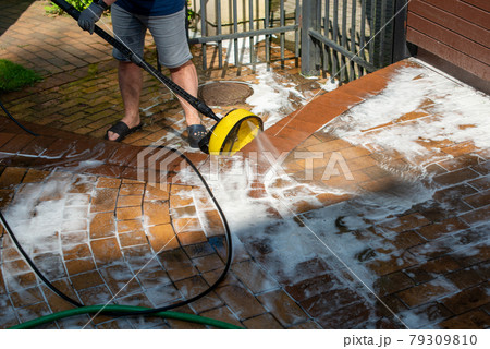 Man cleaning backyard paving tiles with high pressure washer. Man cleaning backyard paving tiles with high pressure washer. 79309810