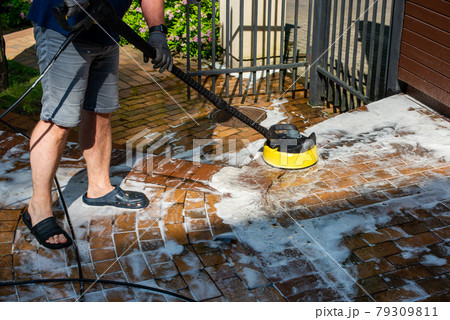 Man cleaning backyard paving tiles with high pressure washer. Man cleaning backyard paving tiles with high pressure washer. 79309811