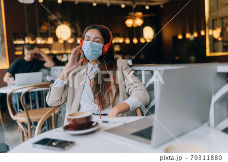 A girl sitting in a coffee shop with headphones. Coronavirus outbreak. A girl sitting in a coffee shop with headphones. Coronavirus outbreak. 79311880