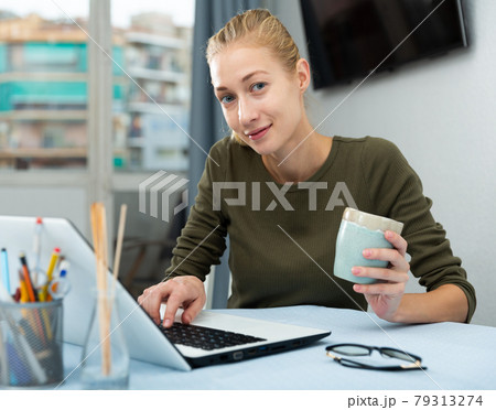 Smiling woman is working with laptop sitting at the table 79313274