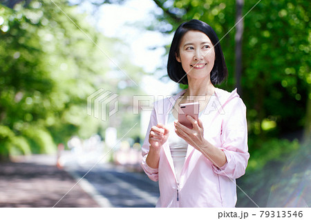 新緑の中スポーツウエアを着てスマホを使用するミドル女性 79313546