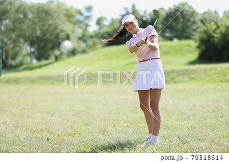 Young woman in sports uniform hitting ball with iron on golf course 79318614