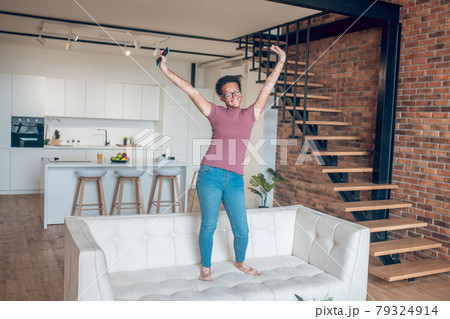 A dark-skinned girl in eyeglasses and with a smartphone at home A dark-skinned girl in eyeglasses and with a smartphone at home 79324914