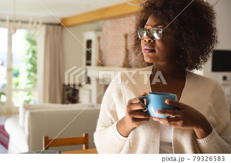 Thoughtful african american woman standing in dining room holding cup of coffee Thoughtful african american woman standing in dining room holding cup of coffee 79326583