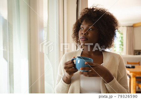 Thoughtful african american woman standing in dining room holding cup of coffee 79326590