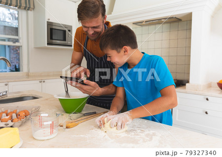 Caucasian father using tablet and son baking and smiling in kitchen 79327340