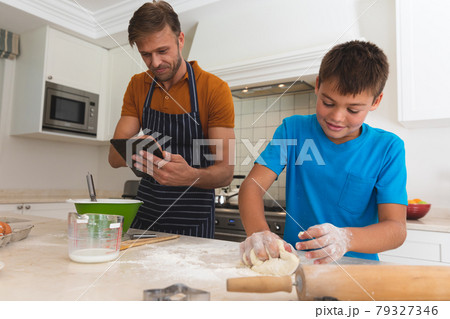 Caucasian father using tablet and son baking and smiling in kitchen 79327346